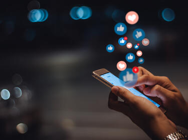 Hands holding a phone with like, love icon bubbles coming from the phone